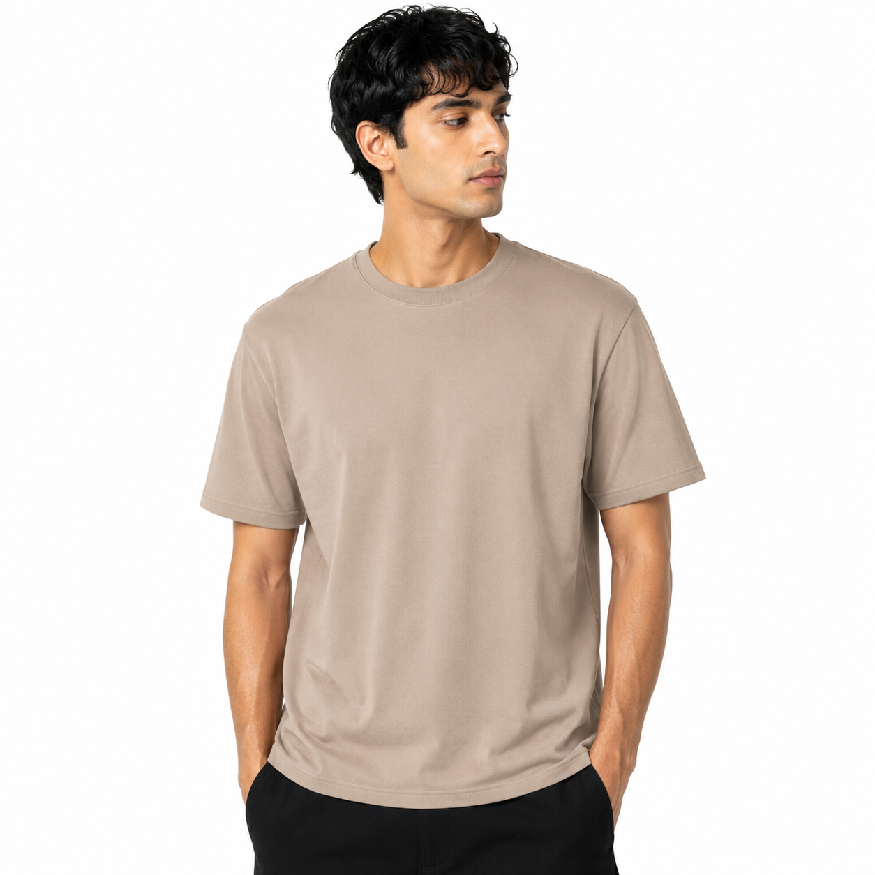 A man wearing a plain short-sleeve crewneck t-shirt in a light taupe-beige color, paired with black pants, photographed against a solid white background.