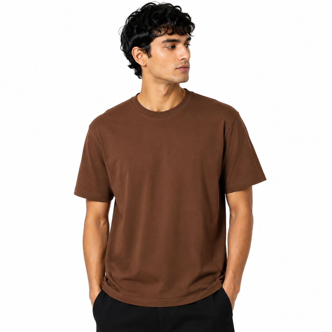 A man wearing a plain brown short-sleeve crewneck t-shirt and black pants, standing against a solid white background.