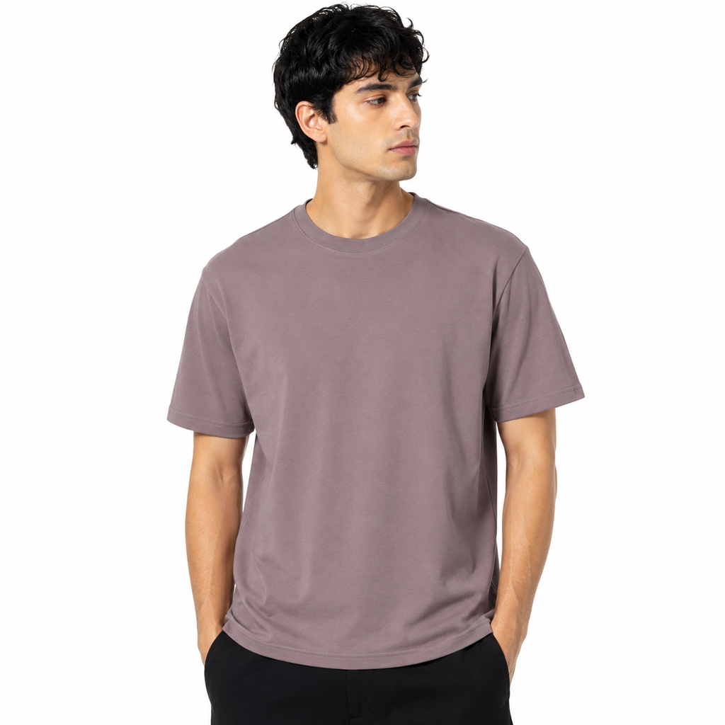 A man wearing a plain crew-neck t-shirt in a muted dusty mauve or taupe color, paired with black pants, photographed against a solid white background.