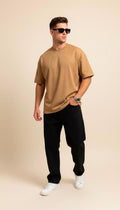 Man wearing a camel color  t-shirt, black pants, and sunglasses on a beige background