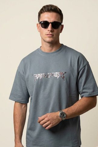 Man wearing a gray t-shirt with a logo, sunglasses, and a watch on a beige background